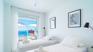 Ein Hotelzimmer mit zwei Betten, einem großen Fenster mit Meerblick und einem gerahmten Bild an der Wand.