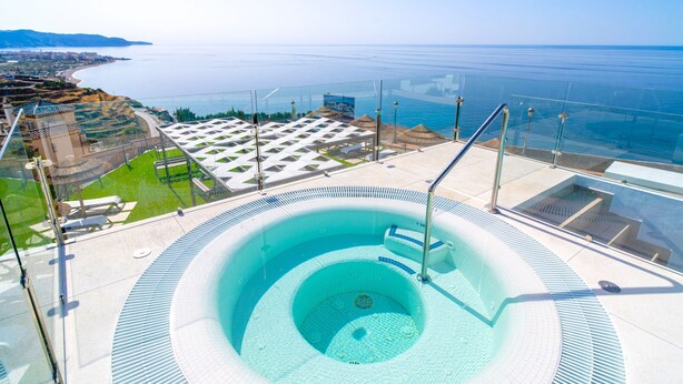 Ein Whirlpool mit weitreichendem Meerblick, umgeben von einem Glasgeländer und einer gefliesten Terrasse.