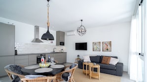 A modern kitchen with grey cabinets, a black pendant light, and a dining area with wicker chairs and a round table. - Casa Solera by Casasol (Nerja)