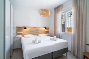 Ein modernes Hotelzimmer mit einem großen Bett, einem Holz-Kopfteil, einer Pendelleuchte und einem Fenster mit Vorhängen.