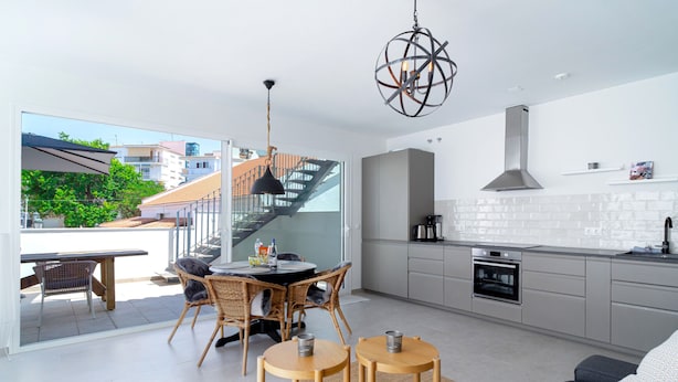 A modern kitchen with a built-in oven, a dining area with wicker chairs, and a staircase leading to an outdoor balcony. - Casa Solera by Casasol (Nerja)