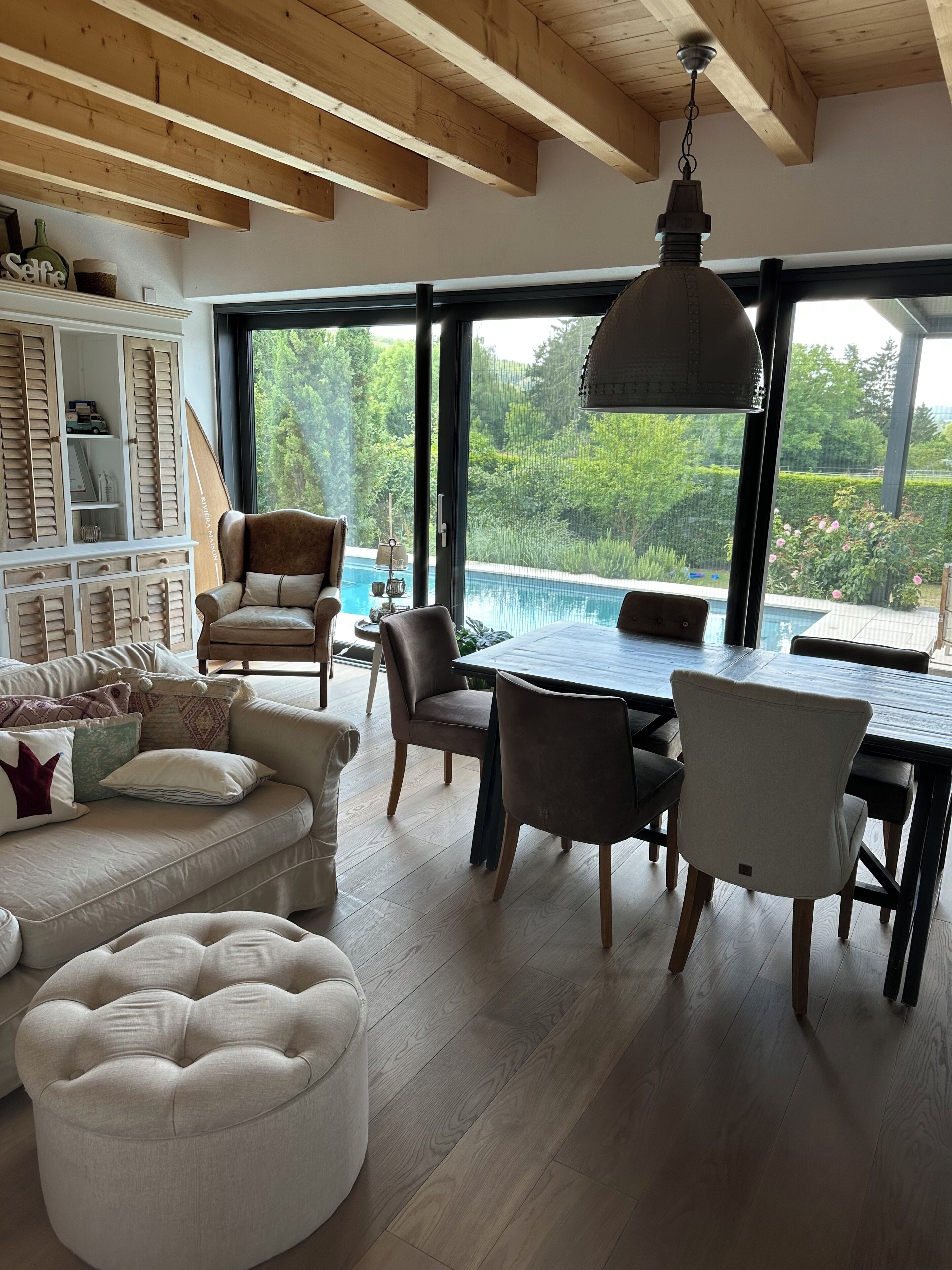 Ein modernes Wohnzimmer mit Essbereich, großen Fenstern und Blick auf einen Swimmingpool.