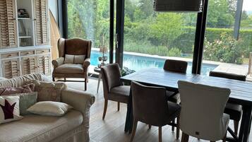 Ein modernes Wohnzimmer mit Essbereich, großen Fenstern und Blick auf einen Swimmingpool.
