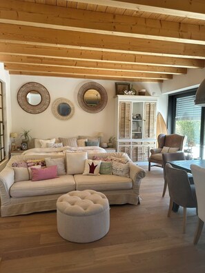 A cozy living room with a wooden ceiling, a sofa set, a round ottoman, and a dining table with chairs.