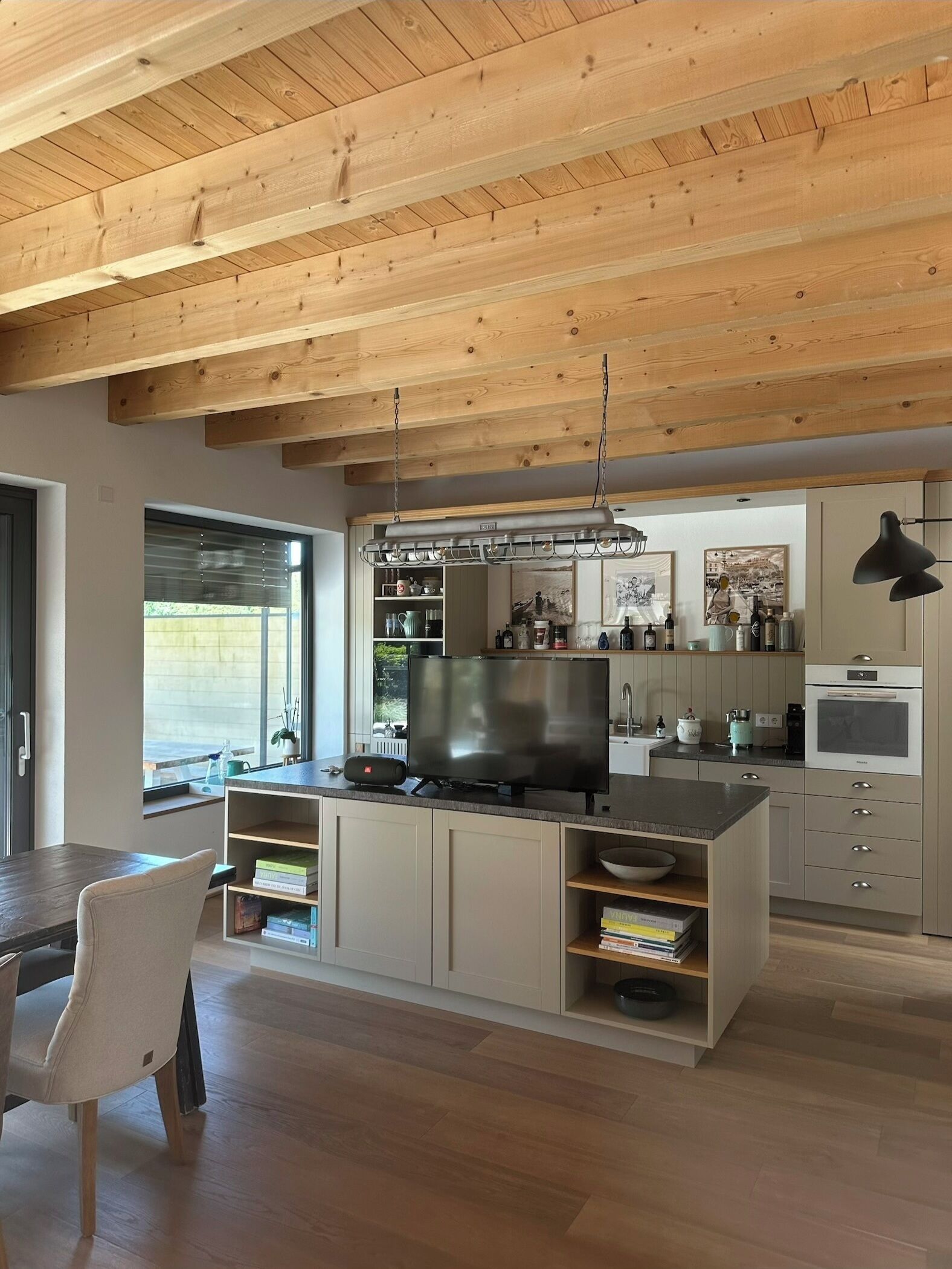 Eine moderne Küche mit Holzbalkendecke, integrierten Geräten und einem Essbereich mit Tisch und Stühlen.