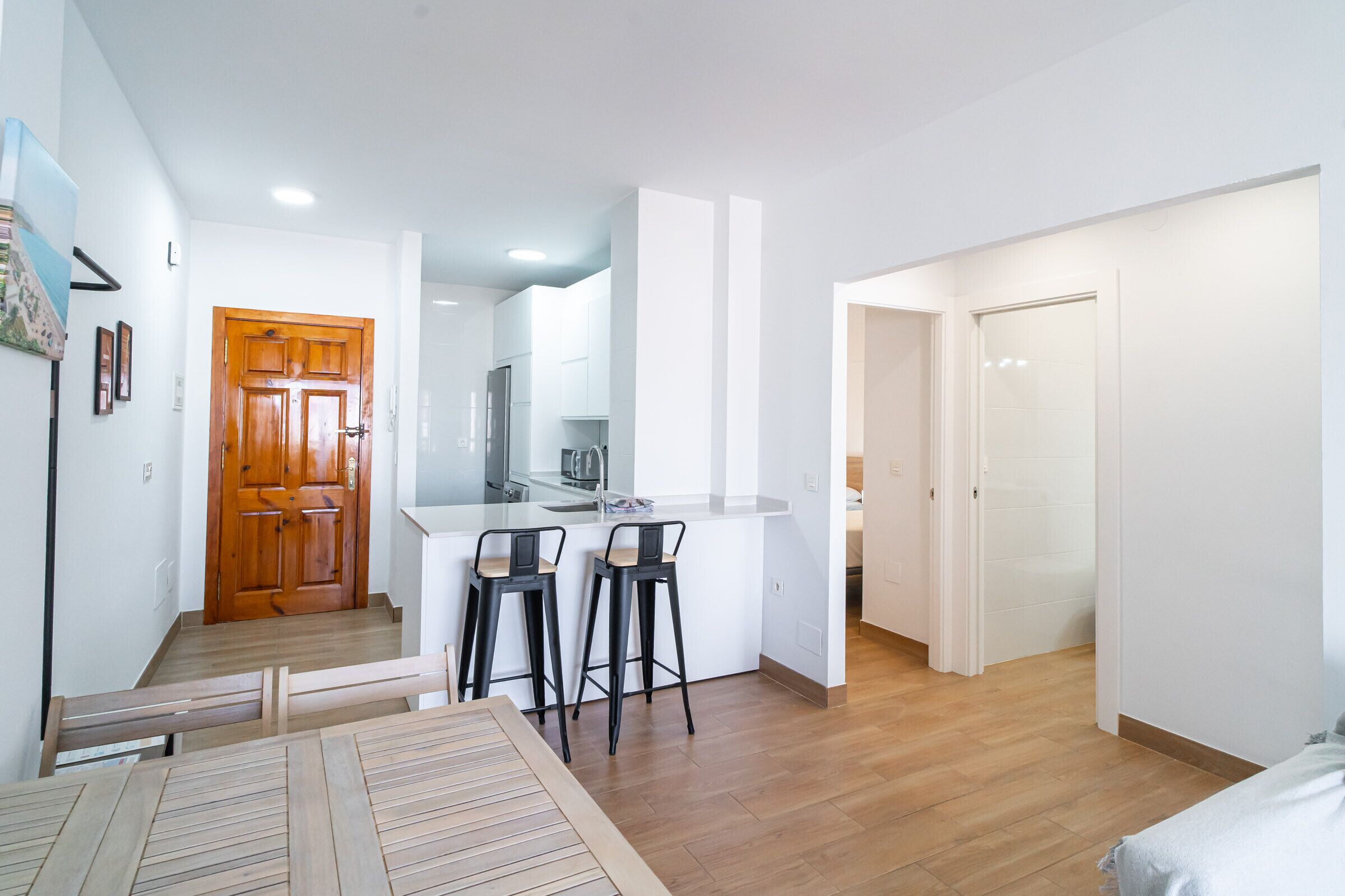 Eine moderne Wohnung mit Küche, zwei Barhocker, einem Holzessttisch und Holzboden.