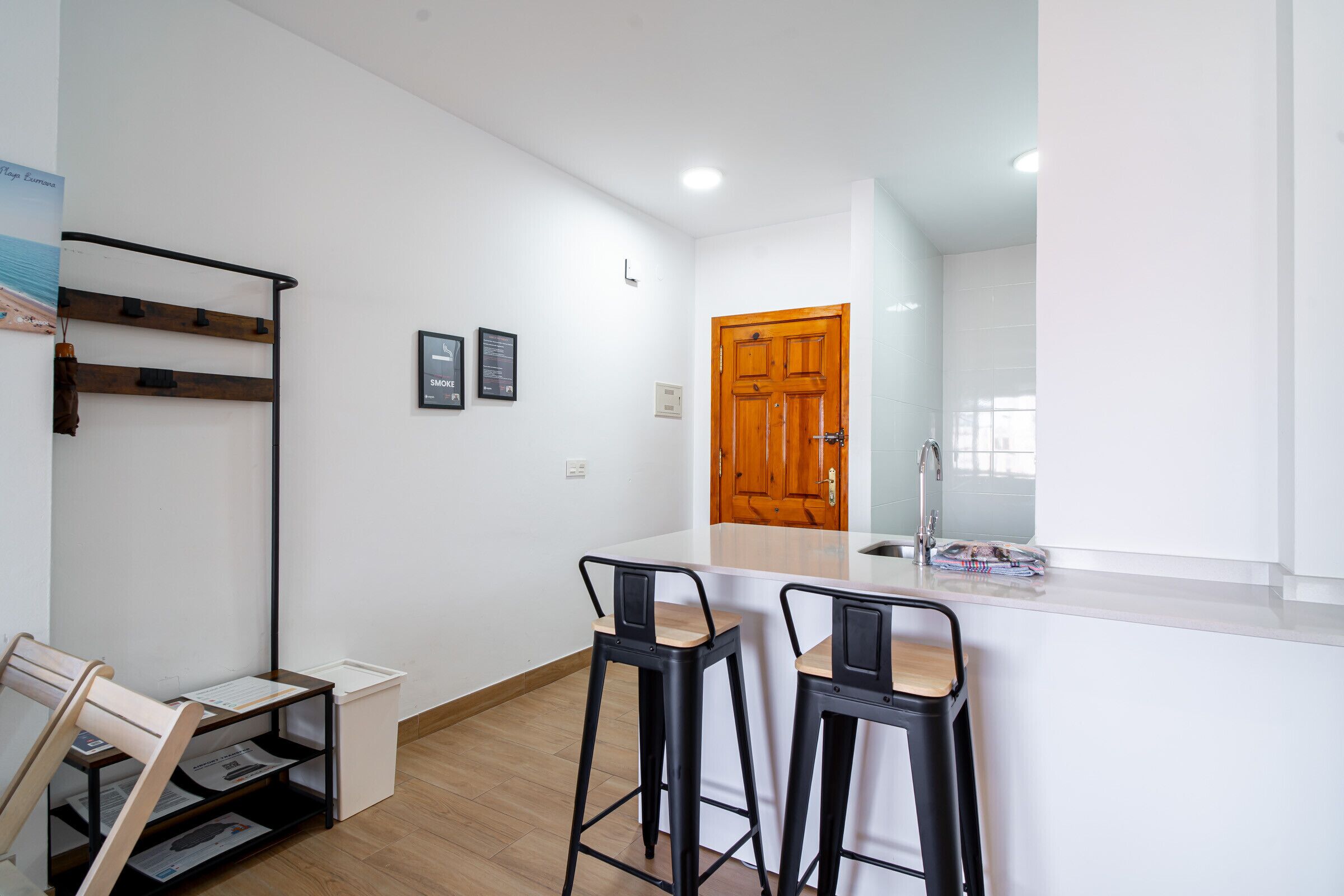 Una cocina moderna con puerta de madera, dos taburetes de bar, encimera blanca y un lavamanos pequeño.