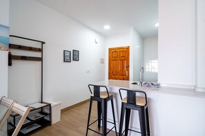 A modern kitchen with a wooden door, two bar stools, a white countertop, and a small sink. - Toboso 2J Torrecilla Beach by Casasol (Nerja)