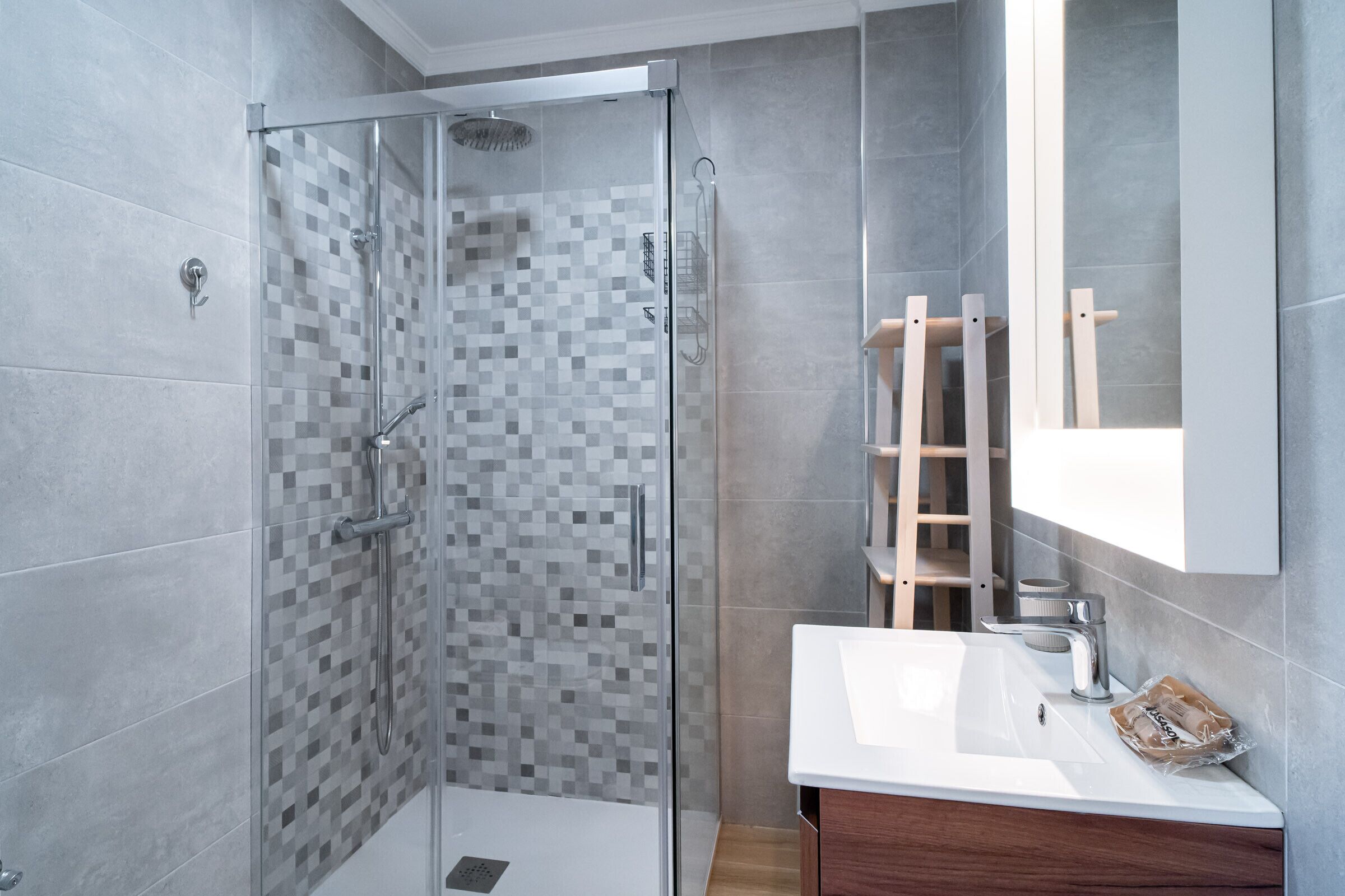 A modern bathroom with a glass-enclosed shower, a wooden ladder, and a white sink.