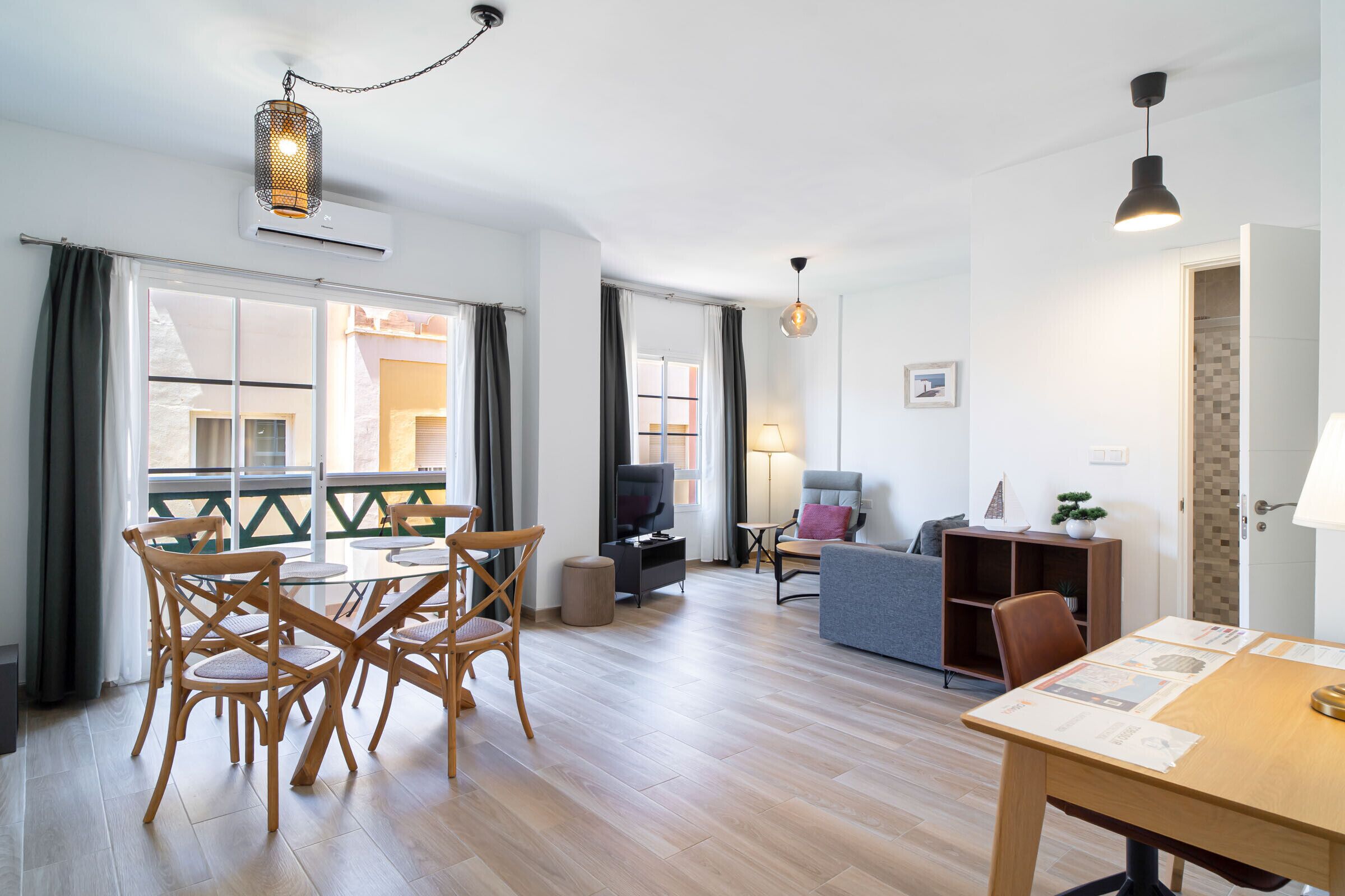 A modern living room with a dining area, a TV, and a small bookshelf.