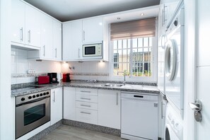 Een moderne keuken met witte kastjes, een inbouwoven, een magnetron, een koffiezetapparaat en een raam met uitzicht.