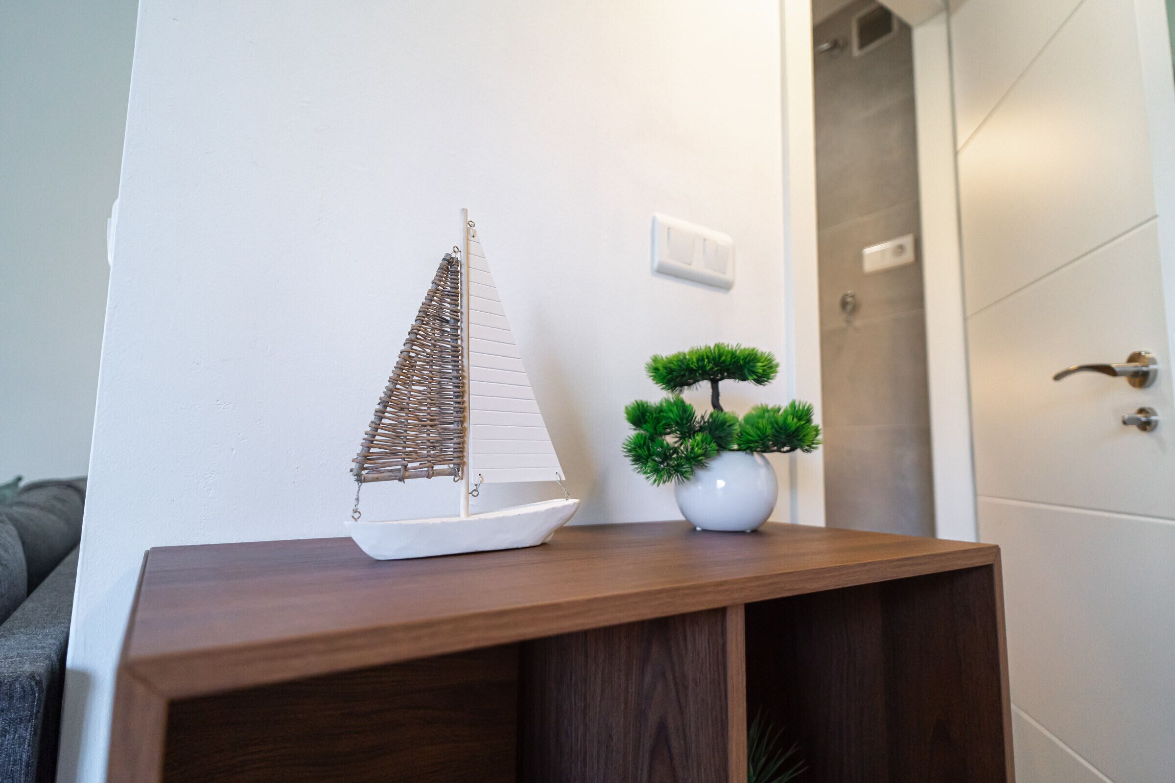 A model sailboat and a bonsai tree on a wooden console table.