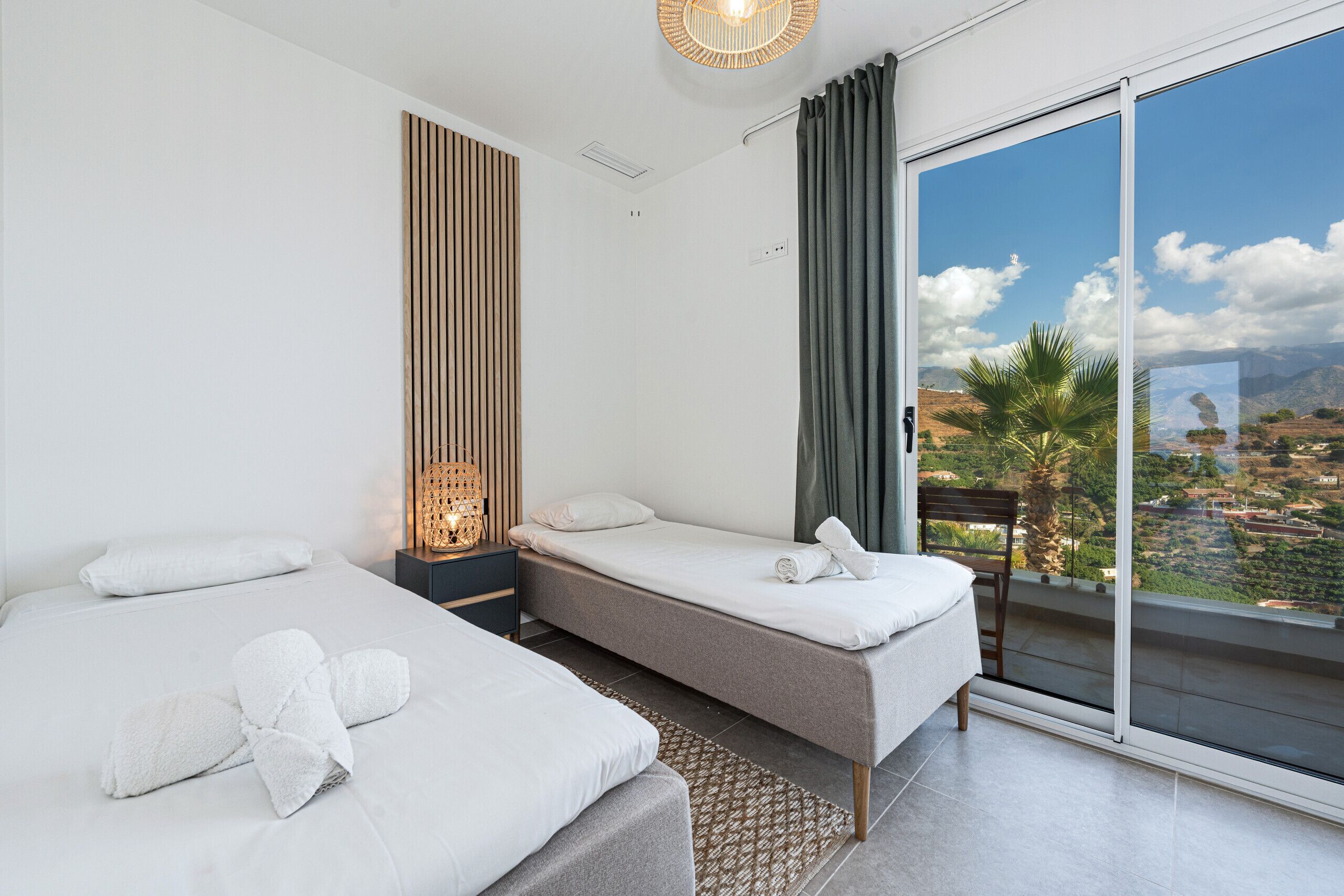 Ein Hotelzimmer mit zwei Betten, Blick auf die Stadt und einem Balkon mit einem Sessel.