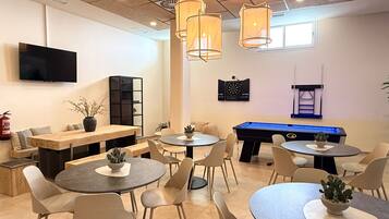Un espace de détente moderne offrant de nombreuses options d’assises, notamment des tables rondes et des canapés, ainsi qu’une table de billard et un jeu de fléchettes.