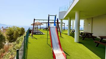 Un terrain de jeux équipé d’un toboggan, de balançoires et de tables de pique-nique, offrant une vue panoramique.