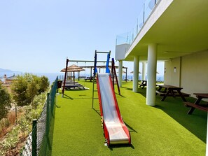 A playground with a slide, swings, and picnic tables, overlooking a scenic view. - Bayview Hills Suite by Casasol (Torrox)
