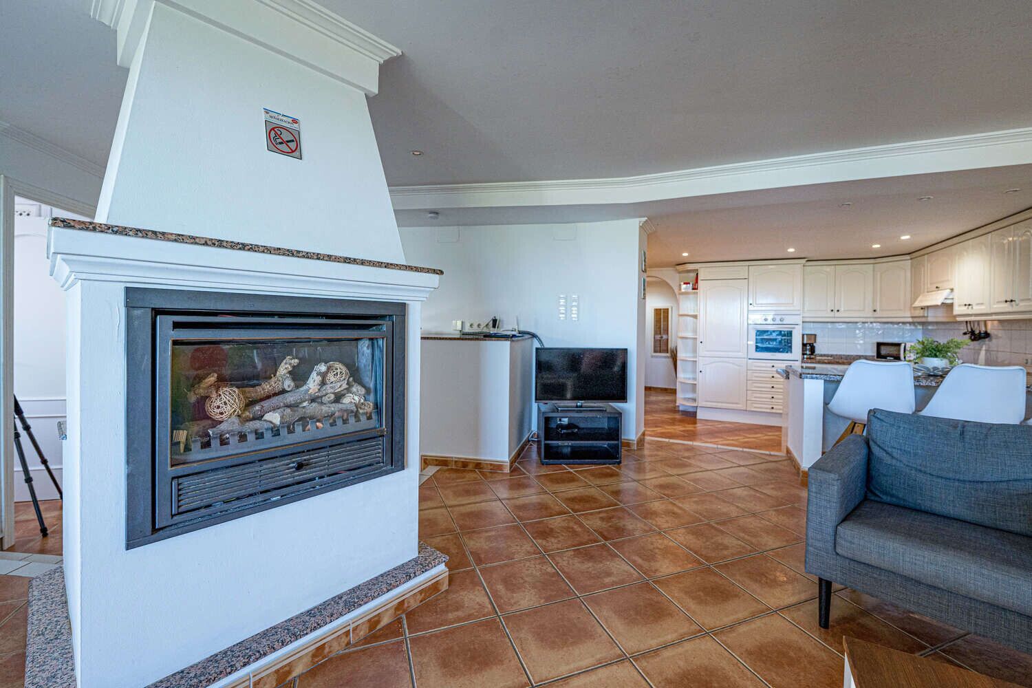 A living room with a fireplace, a television, and a kitchen in the background.