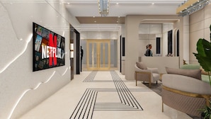 A modern lobby with a large TV screen displaying a Netflix advertisement, a reception desk, and a seating area with a plant. - Hotel Vaarya Inn (Lucknow)
