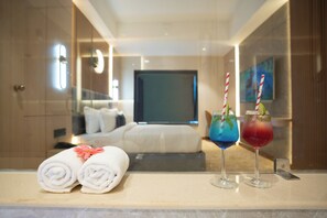 A hotel room with a bed, a TV, a minibar, and two drinks with straws on the counter.