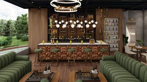 A modern bar area with a wooden bar counter, green upholstered seating, and a view of the outdoors. - Hotel Vaarya Inn (Lucknow)