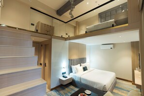 A hotel room with a bed, a desk, a phone, a small table with a fruit plate, and a staircase.