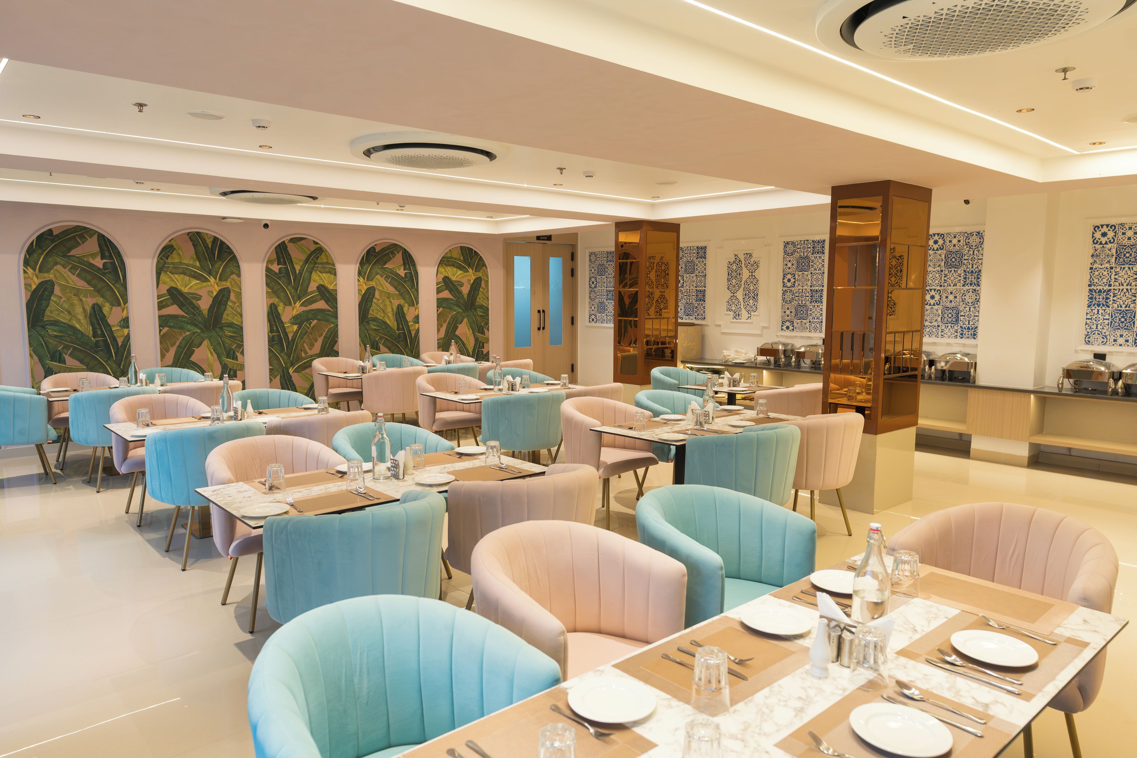 Restaurante com várias mesas, cadeiras, área de cozinha e azulejos decorativos na parede.