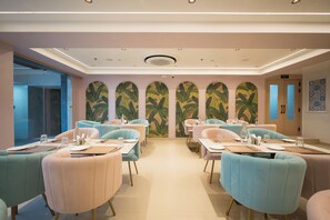 Un restaurant amb seients a caixa i taules, un mural amb fulles tropicals i un sostre amb il·luminació empotrada.