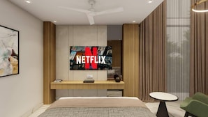 A modern hotel room with a large flat-screen TV mounted on the wall, a bed with a patterned bedspread, a small round table, and a green chair. - Hotel Vaarya Inn (Lucknow)