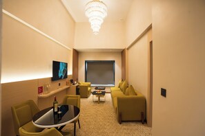 Habitació d'hotel amb televisió de pantalla plana, un penjallum, un sofà, una taula de cafè i una petita taula de menjador amb una ampolla i gots.
