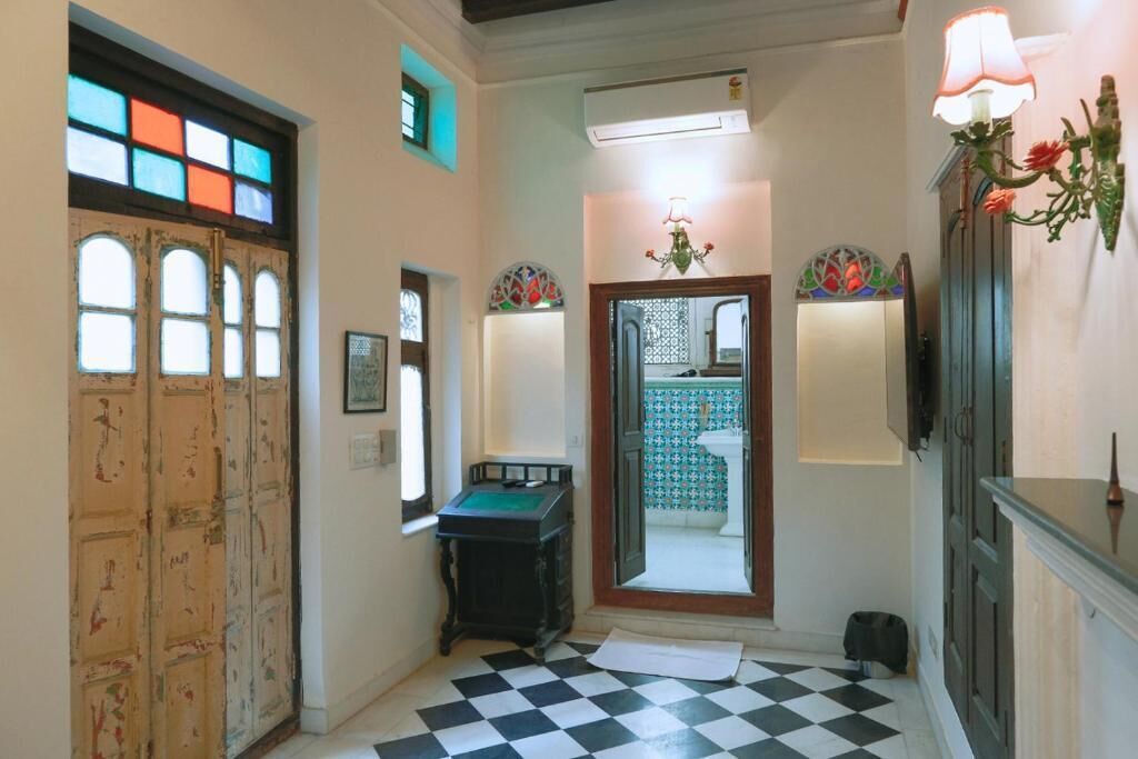 A hallway with a checkered floor, a stained glass door, and a wall-mounted lamp.