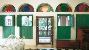 Una habitación con suelo a cuadros, contraventanas verdes, una cama y una puerta que da al exterior.