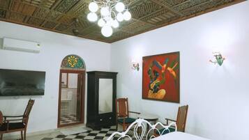 A room with a checkered floor, a bed, a television, a cabinet, and a painting on the wall.