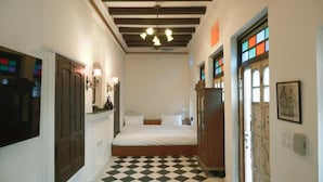 Un pasillo estrecho con piso de cuadros, una cama con ropa de cama blanca y una puerta de madera con vidrieras.