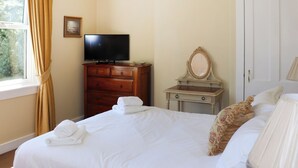 A hotel room with a bed, a dresser with a television, a mirror, and a door. - Heather Cottage - UK52177 (Leven)