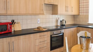 A kitchen with wooden cabinets, a red microwave, a cutting board with a loaf of bread, a kettle, and a table with glasses and a champagne bottle. - Heather Cottage - UK52177 (Leven)