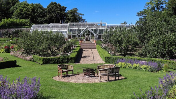 A greenhouse with a glass roof, surrounded by manicured gardens and benches. - Heather Cottage - UK52177 (Leven)
