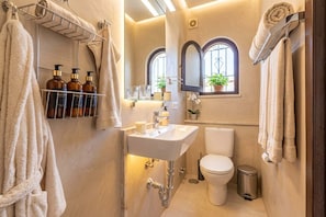 A compact bathroom with a white sink, a toilet, and a shower area. There are towels hanging on a rack and a potted plant on the windowsill. - Casa Lavanda - Hacienda 37 by Casasol (Nerja)