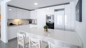 Une cuisine moderne avec des meubles blancs, un îlot central doté de chaises, un four à micro-ondes et un réfrigérateur.