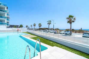 A swimming pool with a metal ladder, a parking lot with cars, palm trees, and a building with balconies. - Duna Beach Torrox Costa by Casasol (Torrox)