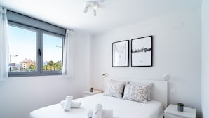 Une chambre d’hôtel moderne avec un grand lit, deux tableaux encadrés au mur, une table de chevet avec une plante et une fenêtre avec des rideaux.