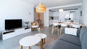 Un salon moderne doté d’un téléviseur à écran plat, d’un canapé, d’une table basse et d’un coin repas avec des chaises et une table.