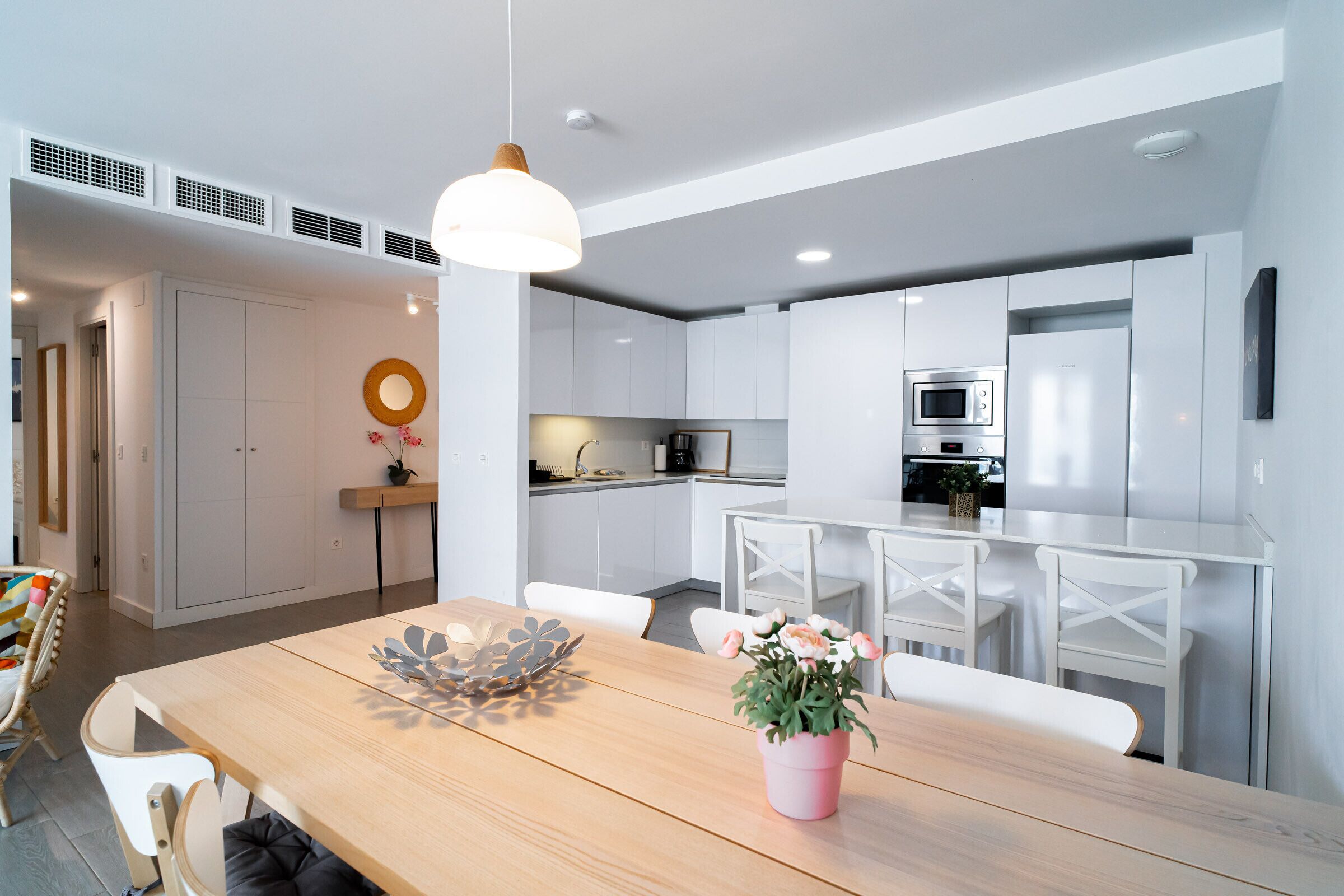Una cocina moderna con armarios blancos, una mesa de comedor de madera y un centro de mesa con flores rosas.