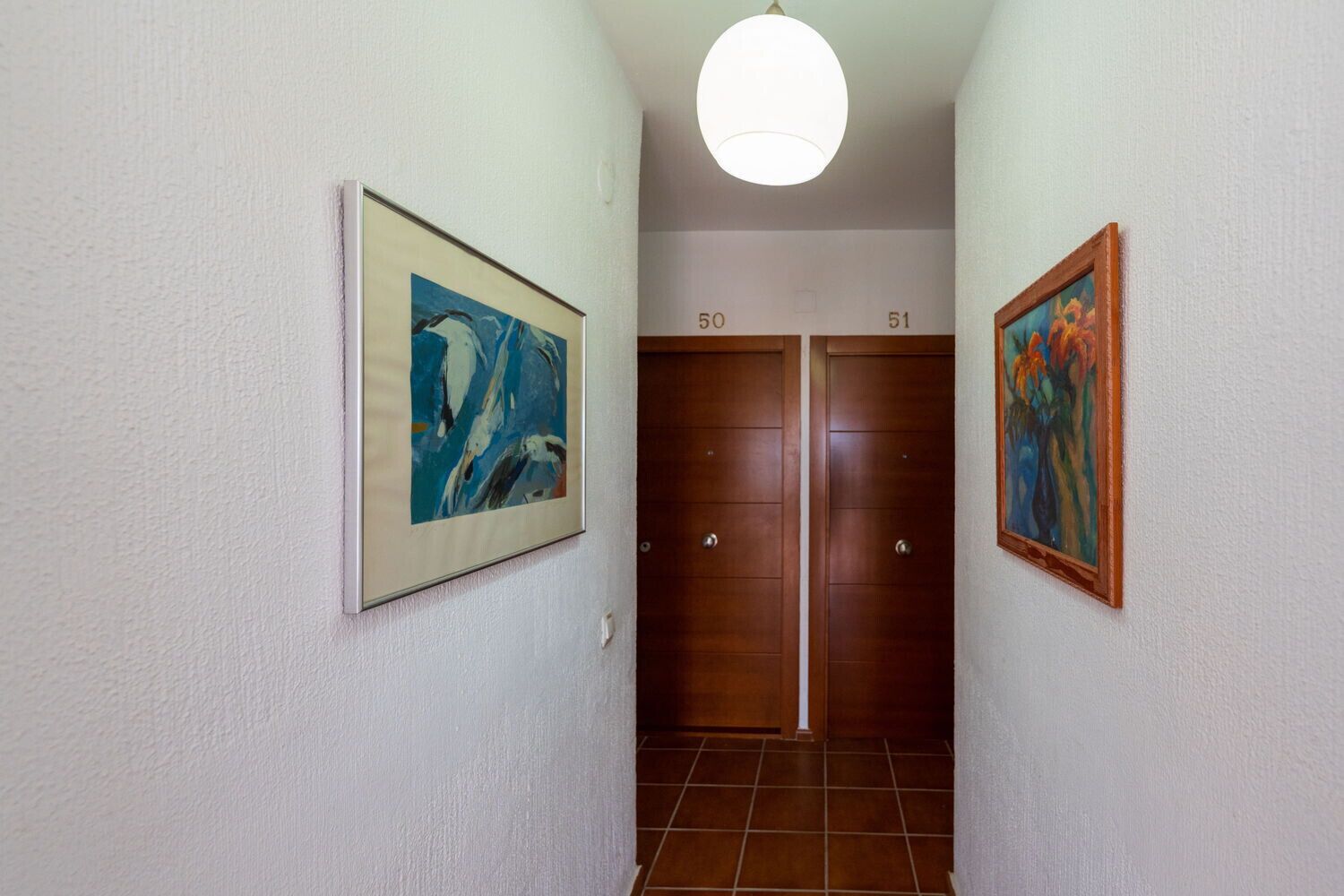 A hallway with two wooden doors labeled 50 and 51, flanked by two framed abstract paintings.
