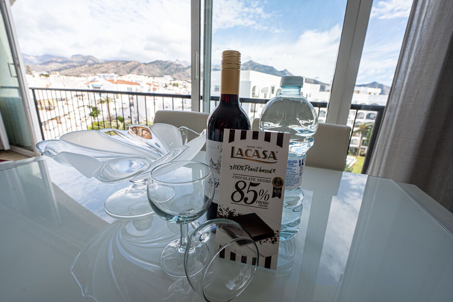 Una mesa con una botella de licor de chocolate IACASA, una botella de agua y copas de vino.