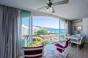 Un balcón con vista al mar y edificios, un comedor con mesa y sillas, y un ventilador de techo.