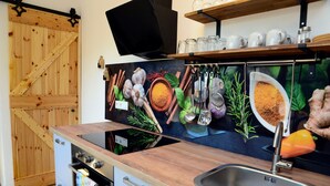 Une cuisine avec une porte en bois, un poêle, un évier et un téléviseur fixé au mur.
