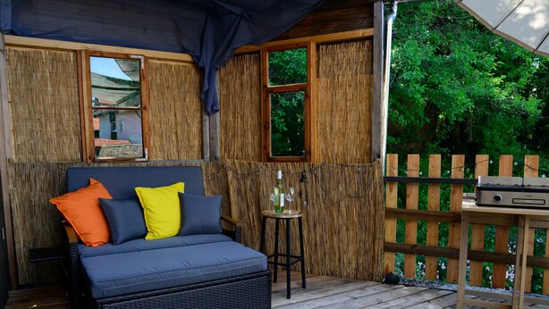 Une terrasse en bois avec un canapé en osier, une petite table et un barbecue.