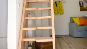 Un escalier en bois dans un cadre résidentiel, avec une cuisine et un salon en arrière-plan.