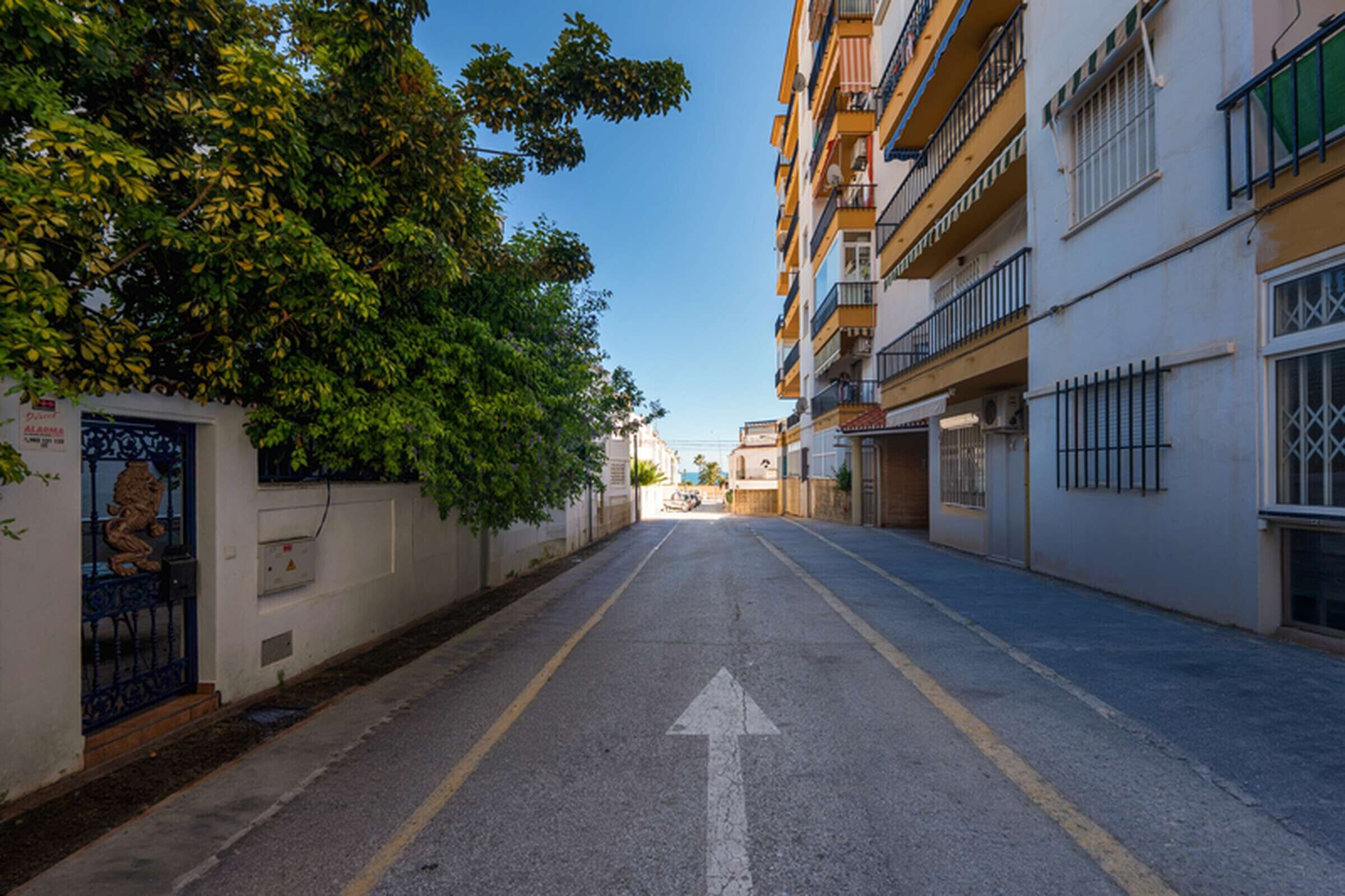 Una calle urbana estrecha con una vía despejada, una flecha direccional y un edificio con balcones.