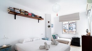 Ein Schlafzimmer mit einem großen Bett, einem Nachttisch, einem Bücherregal, einem Fenster mit Blick und einer Hängeleuchte.
